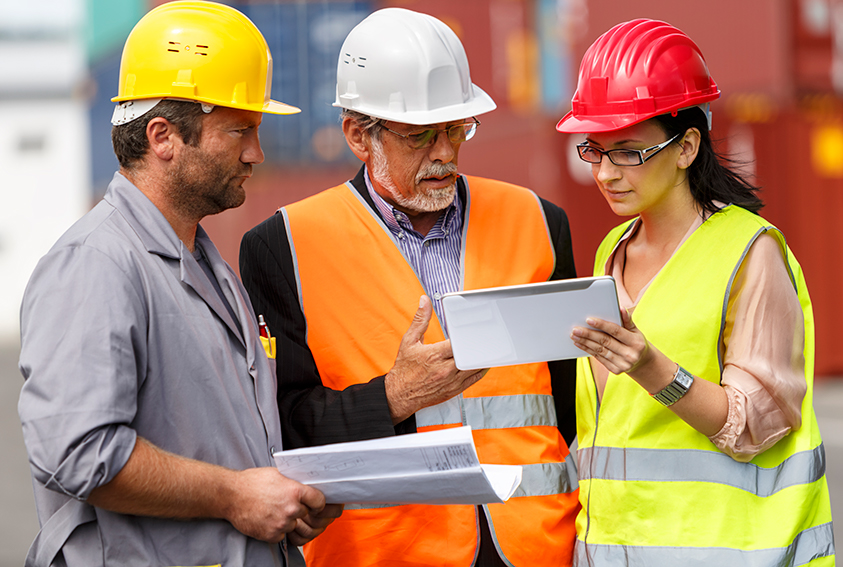 3 people wearing hardhats looking at a tablet and discussing